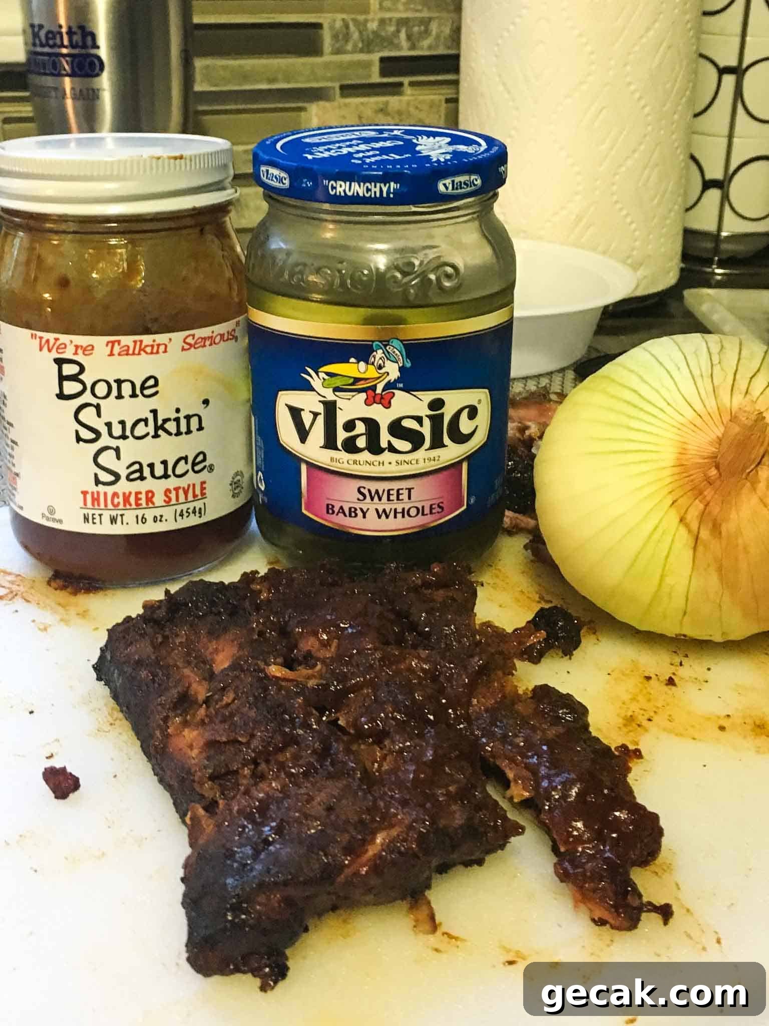 ribs sitting in front of BBQ sauce pickles and onion close up view