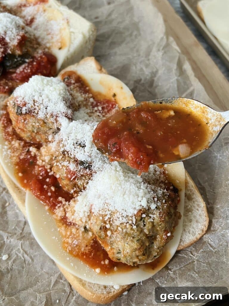 Building a meatball parm sub with turkey pesto meatballs, tomato basil sauce, provolone and pecorino cheese on a long roll.