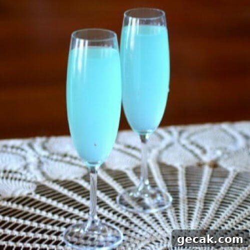 Two champagne glasses with sparkling light blue cocktail in them.