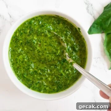 A top down view of a bowl of basil sauce with a spoon in it.