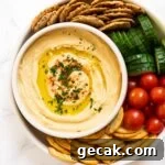 Creamy Chickpea Hummus Recipe: Classic Homemade Dip 13 a top down view of a bowl of chickpea hummus surrounded by crackers and veggies.