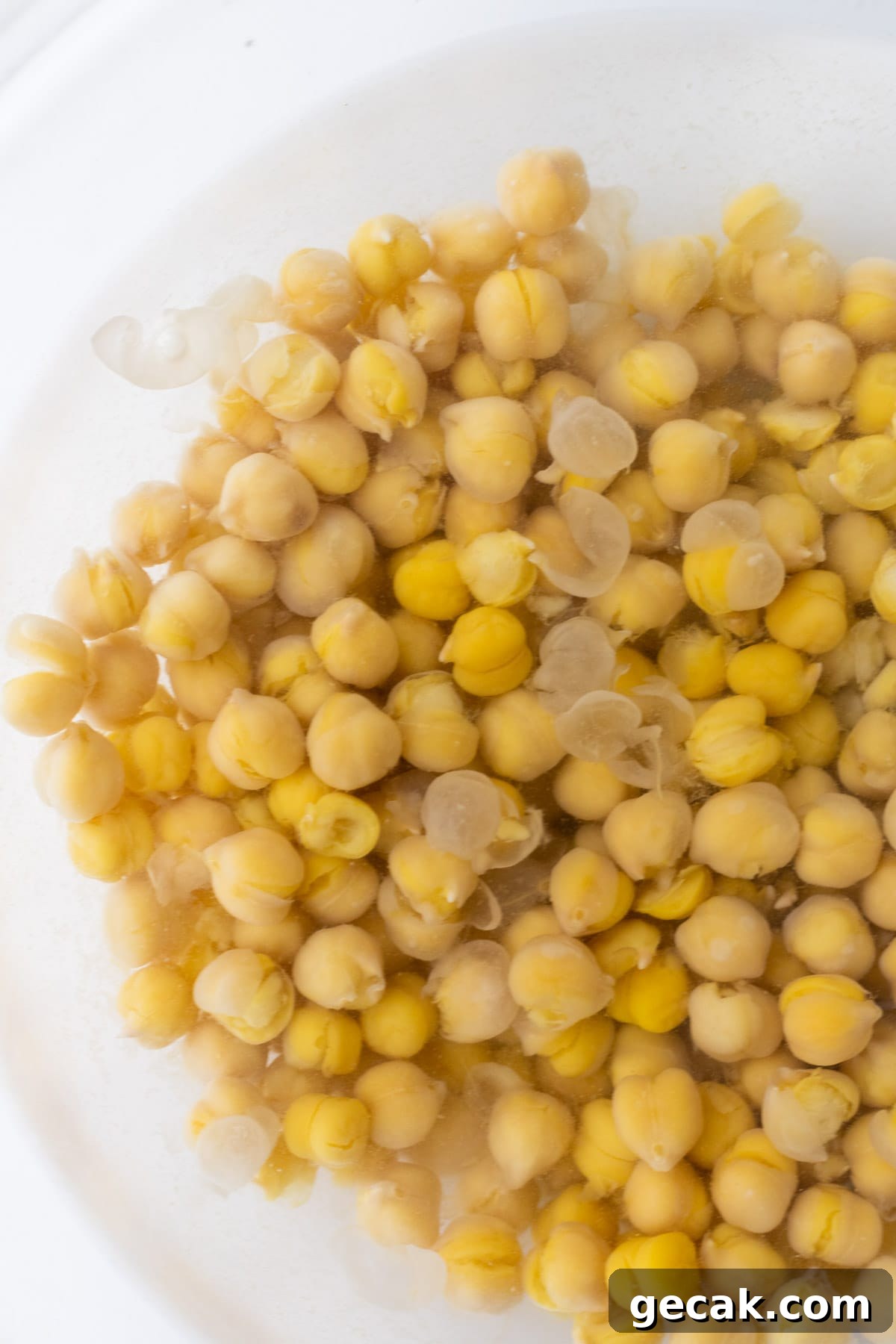 Creamy Chickpea Hummus Recipe: Classic Homemade Dip 5 Cooked chickpeas in a bowl of water with skins floating in it.
