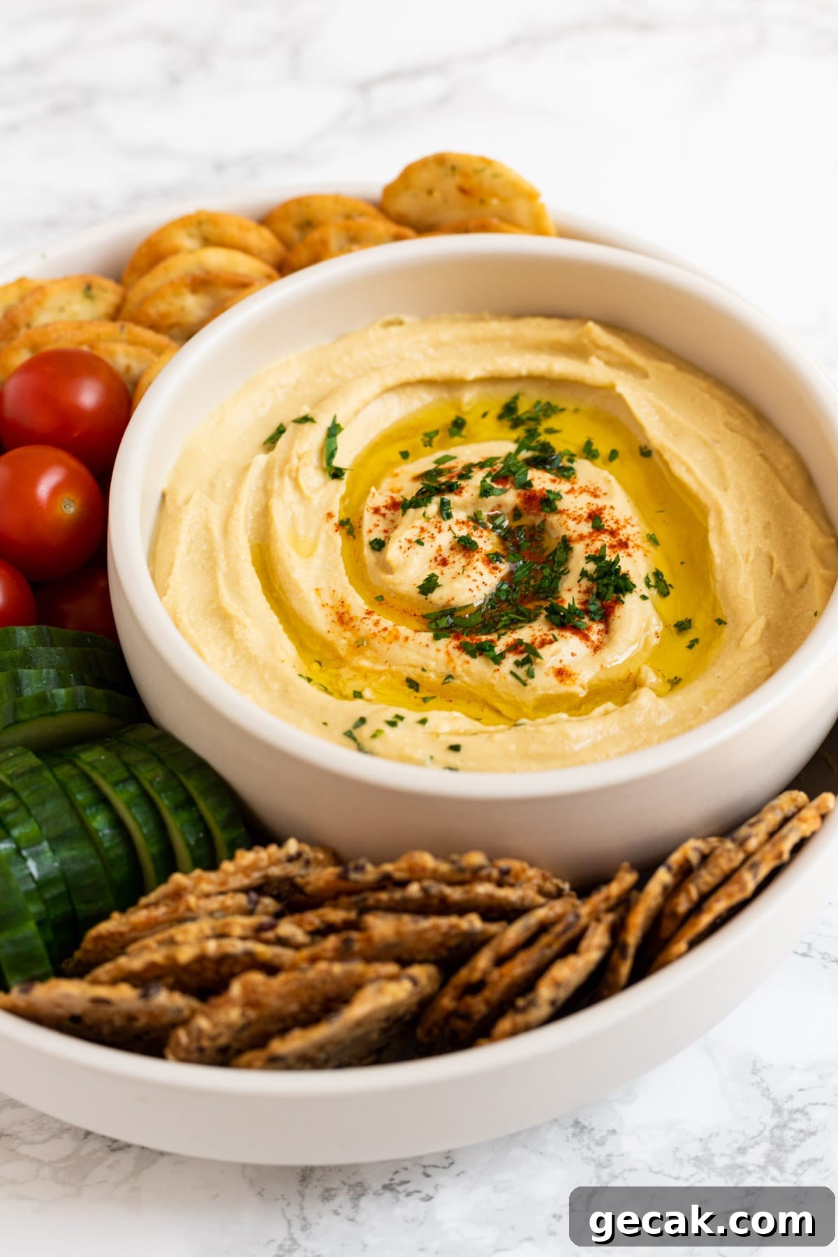 Creamy Chickpea Hummus Recipe: Classic Homemade Dip 8 A side view of a bowl of hummus surrounded by veggies and crackers.