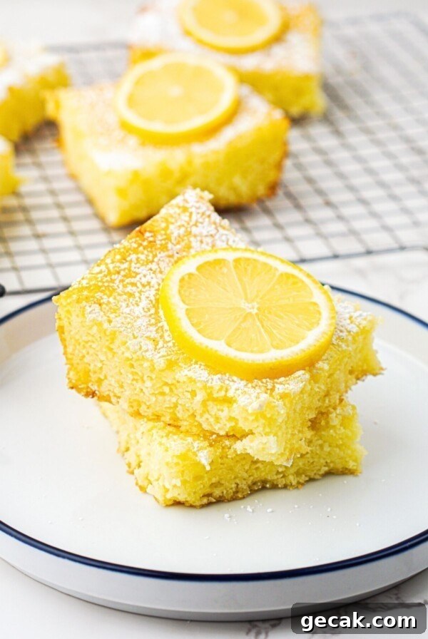 Bright yellow lemon bars stacked on a small white plate with a slice of lemon on top.