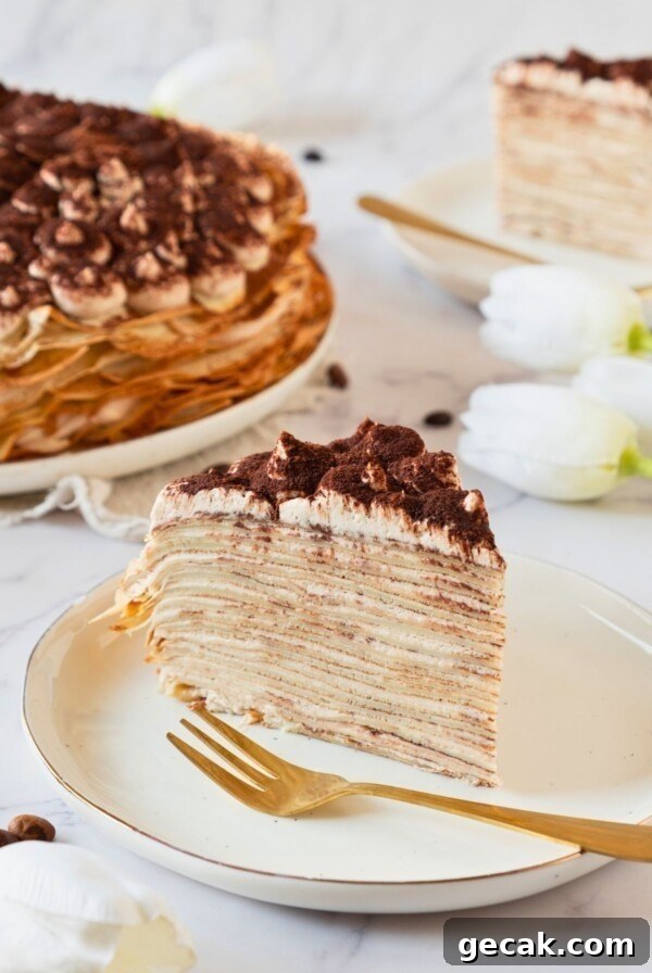 Golden light and fluffy slice of cake made from layers of thin crepes, served on a white plate.