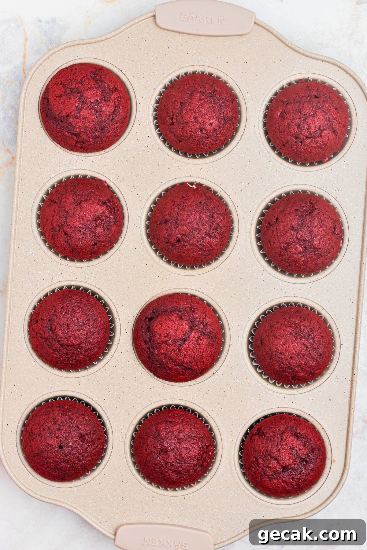 Bright red velvet cupcakes in a muffin tin after being baked.
