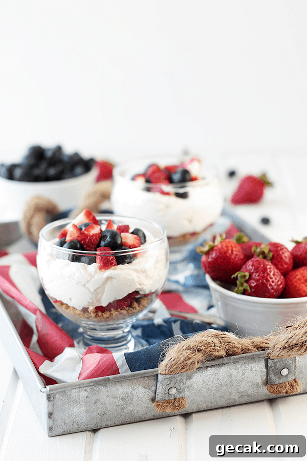 No-Bake Berry Cheesecake Parfait Recipe with Layered Berries 3 a couple bowls of cheesecake parfait with berries served on a tray with American flag decor and bowls of fresh berries