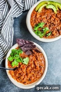 Two white bowls of veggie chili on a blue counter with a striped towel next to them.