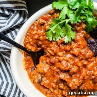 Chili in a white bowl on a blue counter with black spoon sticking out.