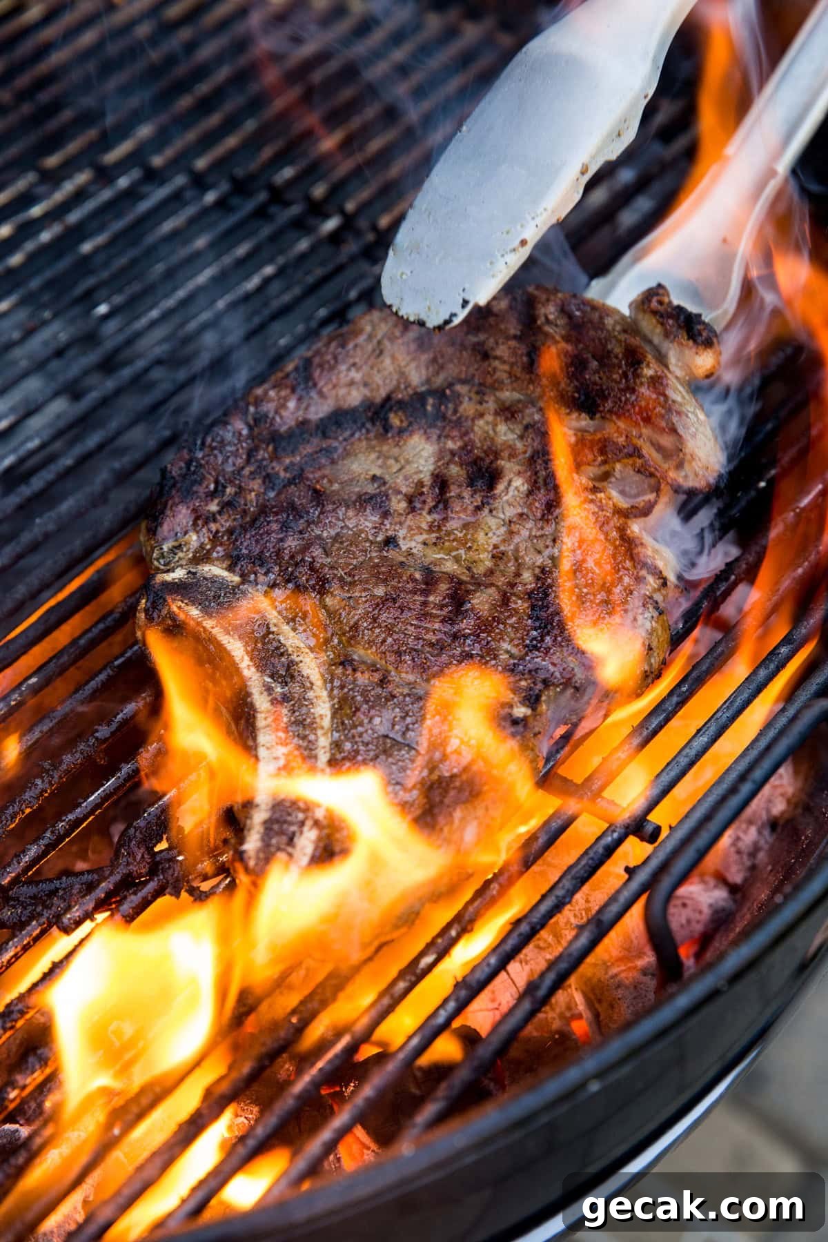 How to Grill the Perfect Steak Every Time 2 Steak being flipped by metal tongs on a charcoal grill with a large fire flare up.