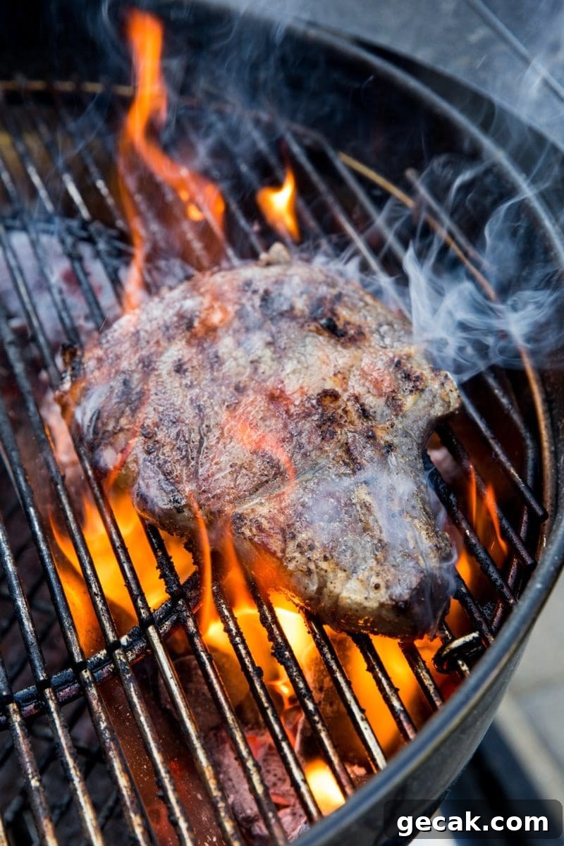 How to Grill the Perfect Steak Every Time 13 Grilling steak on a charcoal grill with a large flare up, flames engulfing the steak.