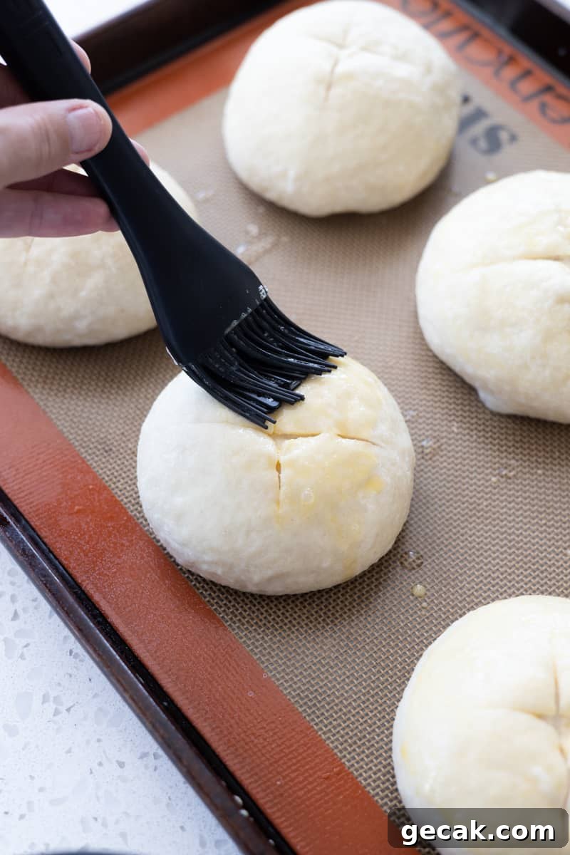 A brush putting egg wash on each bun. 
