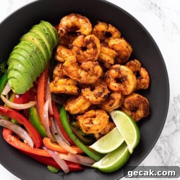 a top down view of a serving bowl with shrimp, sautéed veggies, sliced avocado and limes.