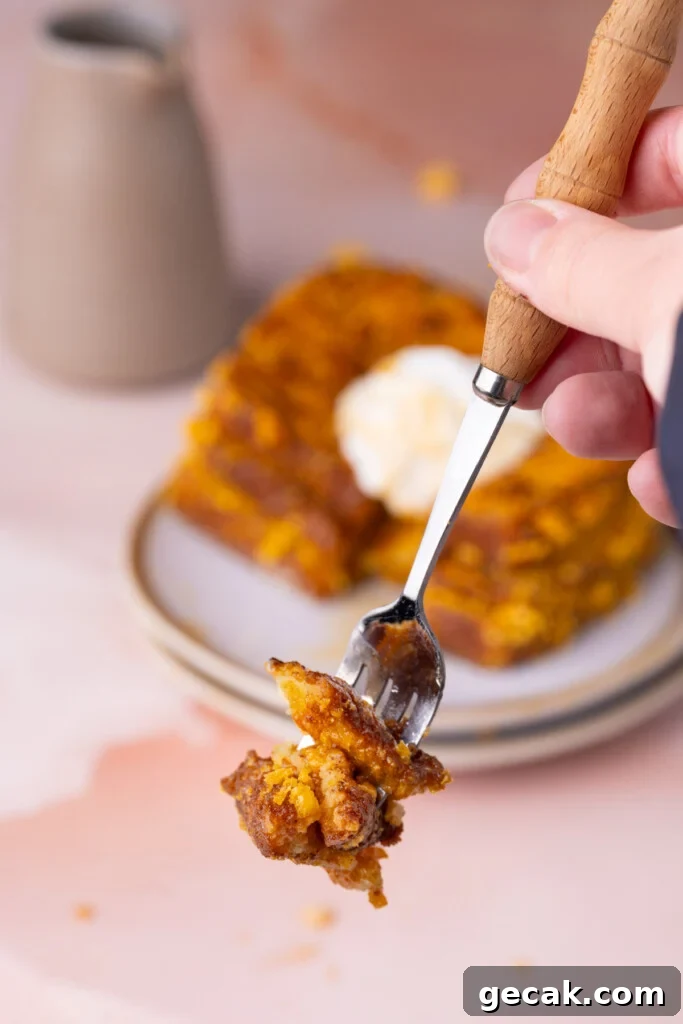 25-Minute Crunchy Cap'n Crunch French Toast Recipe 2 Holding up a forkful of crispy Cap'n Crunch French Toast to the camera with a full stack topped with whipped cream in the background.