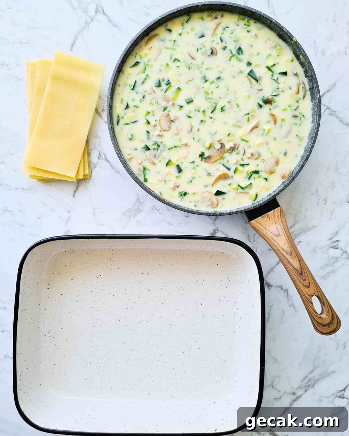 A pan of creamy chicken and vegetable filling next to a stack of lasagna sheets and baking dish