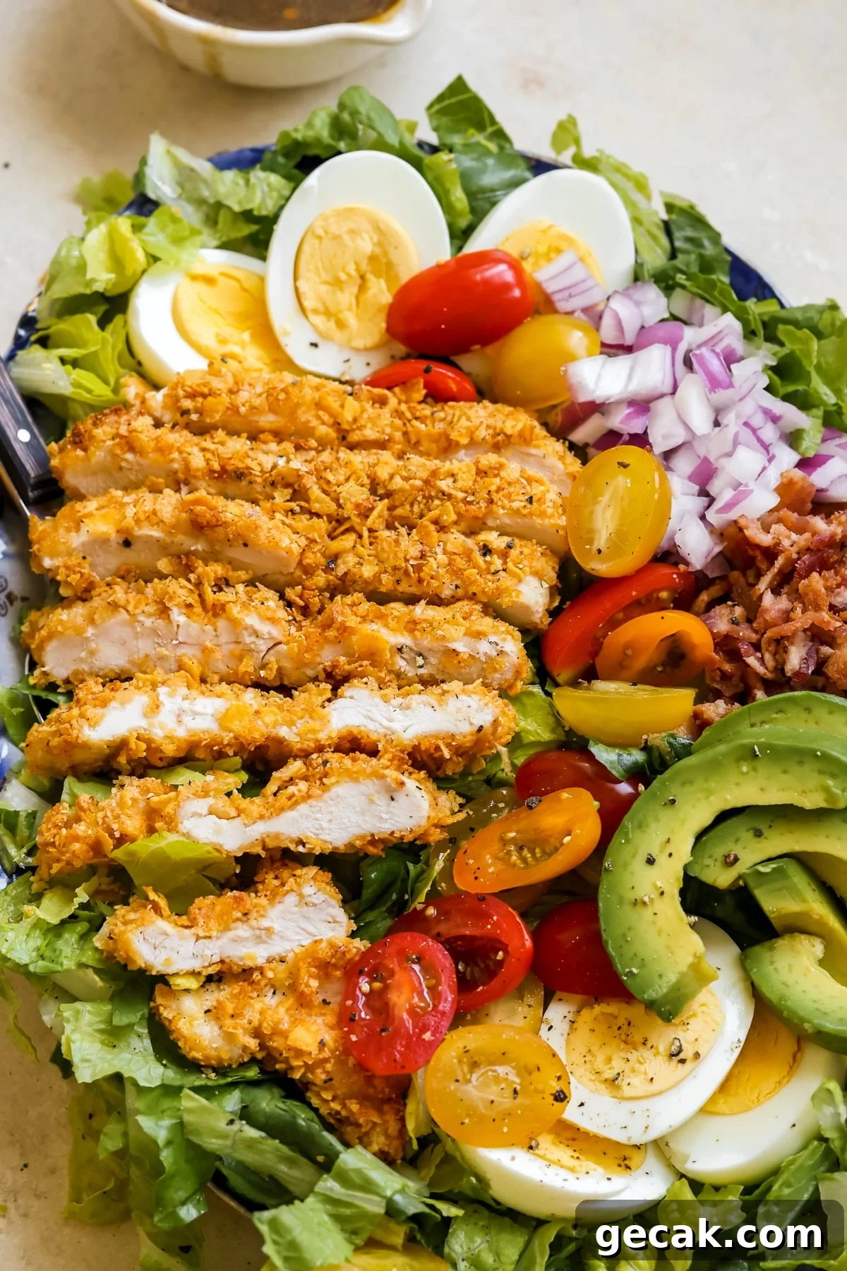 romaine lettuce, chicken, avocado, red onion, tomatoes, eggs and bacon on a platter with black pepper on top. 