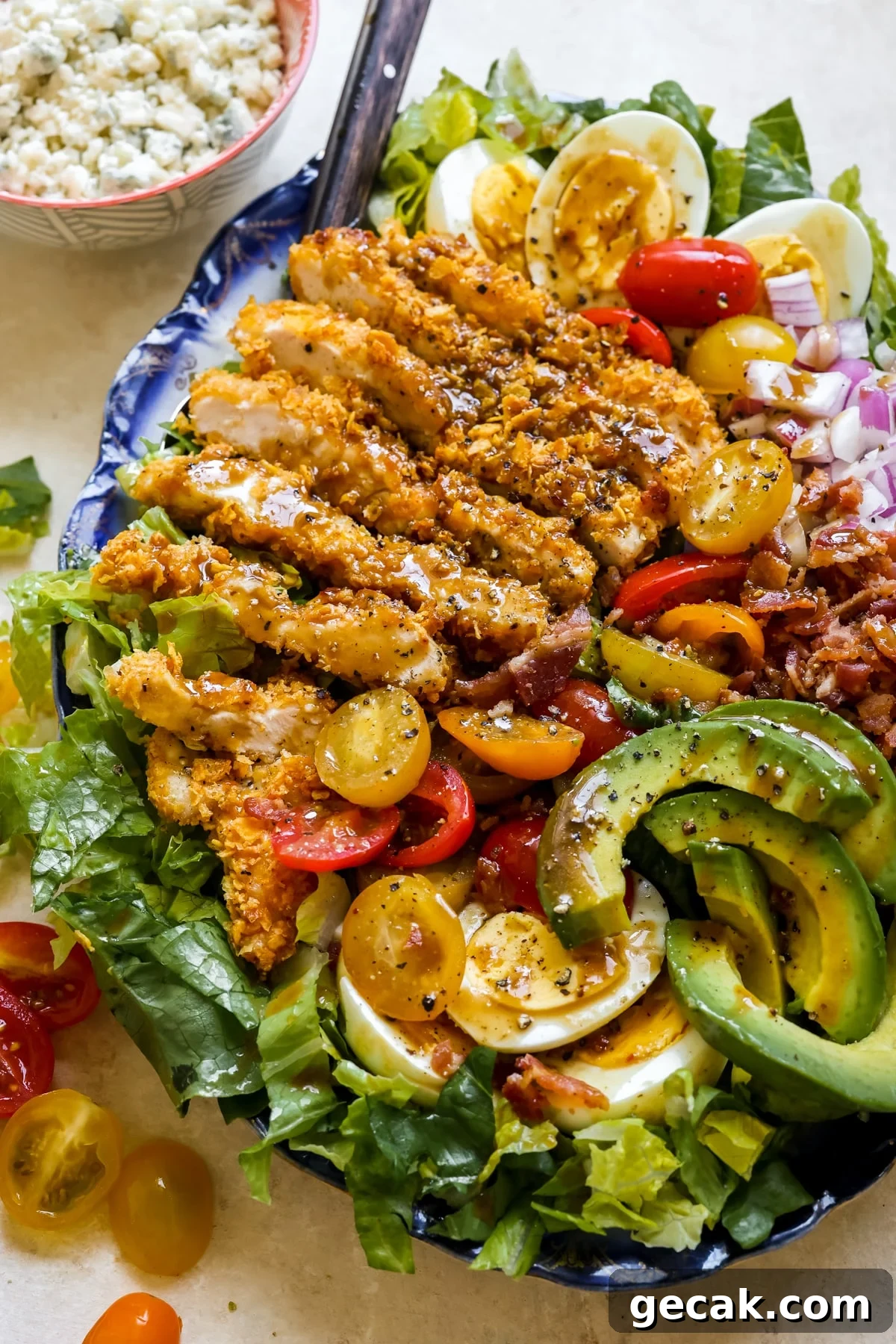 a cobb salad on a blue platter with dressing on top and crispy chicken. 