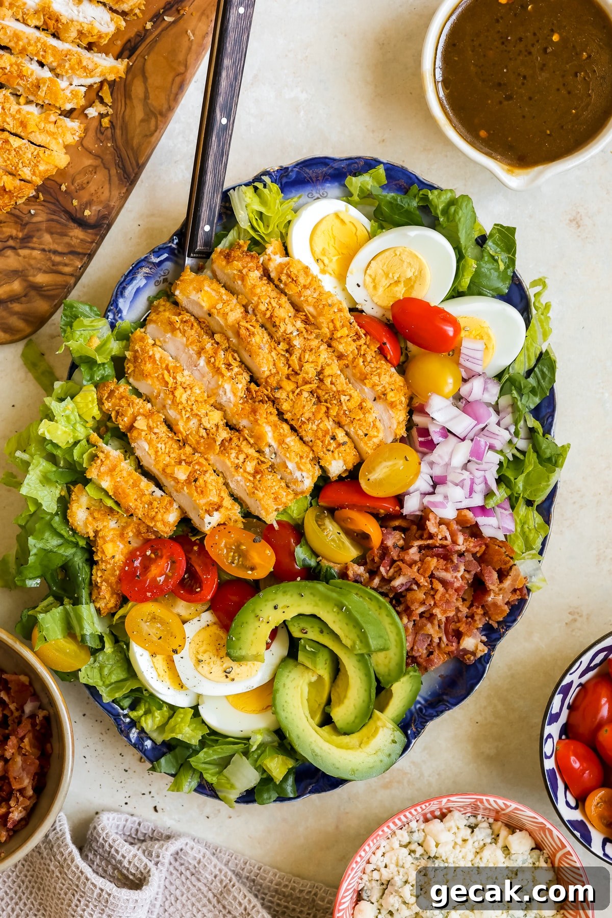 a cobb salad on a blue platter with crispy chicken and dressing on the side. 