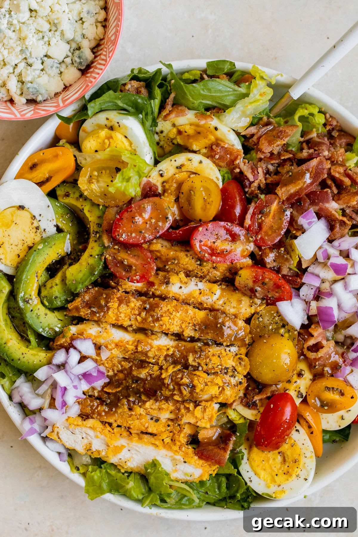 a cobb salad in a white bowl with dressing on top and crispy chicken. 