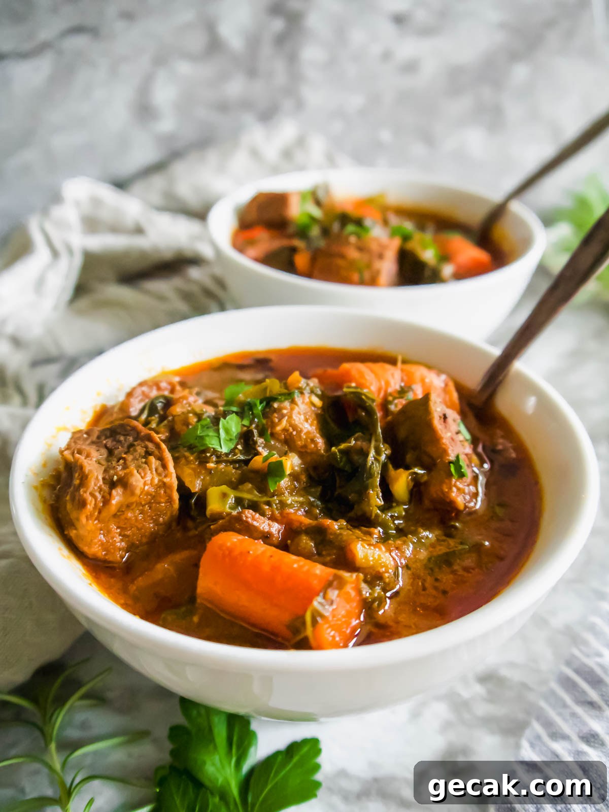 Side angle of beef and kale stew in two bowls with spoons inside them.