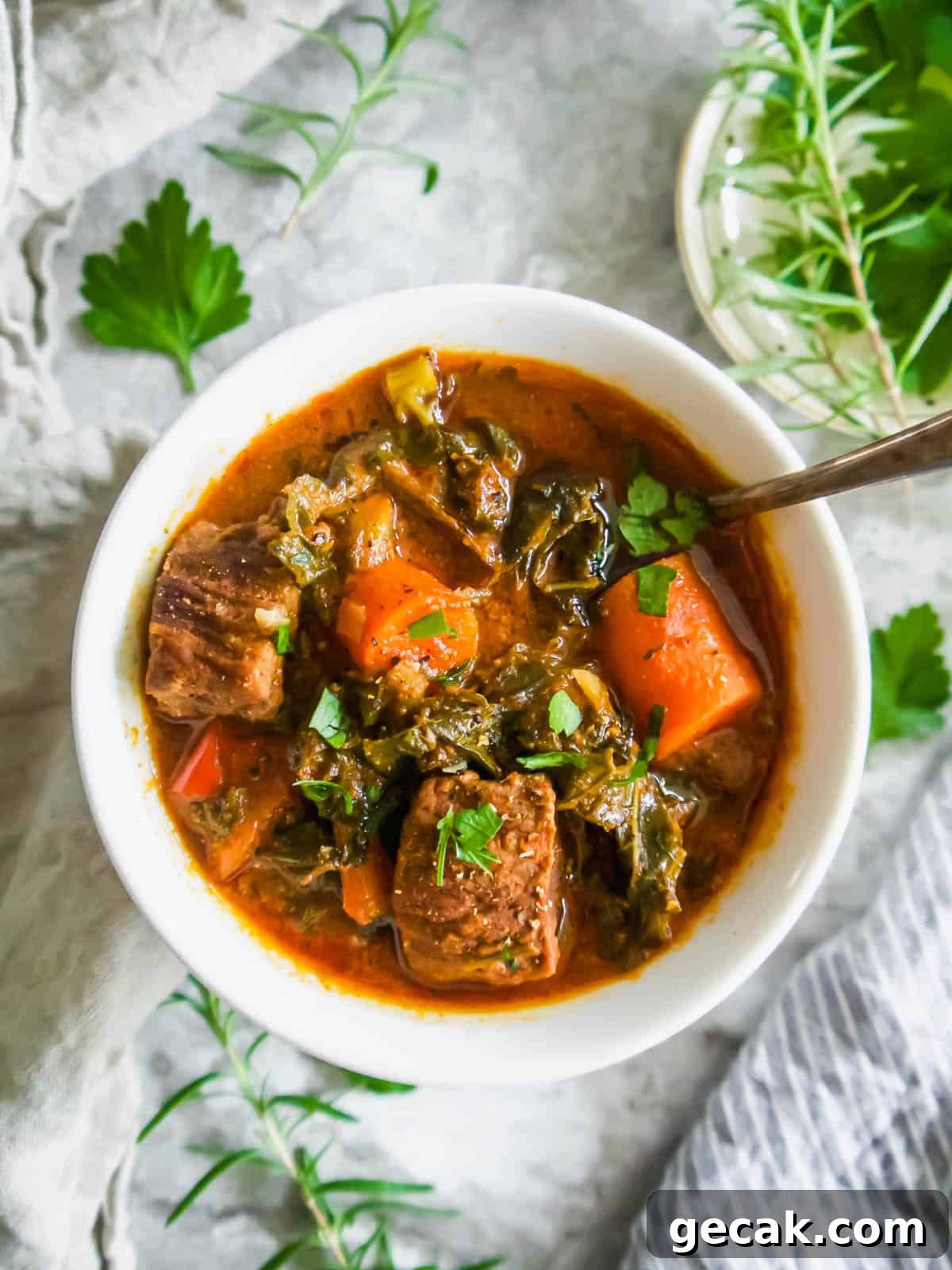 Beef Kale and tomato stew in a large bowl with a spoon in it.