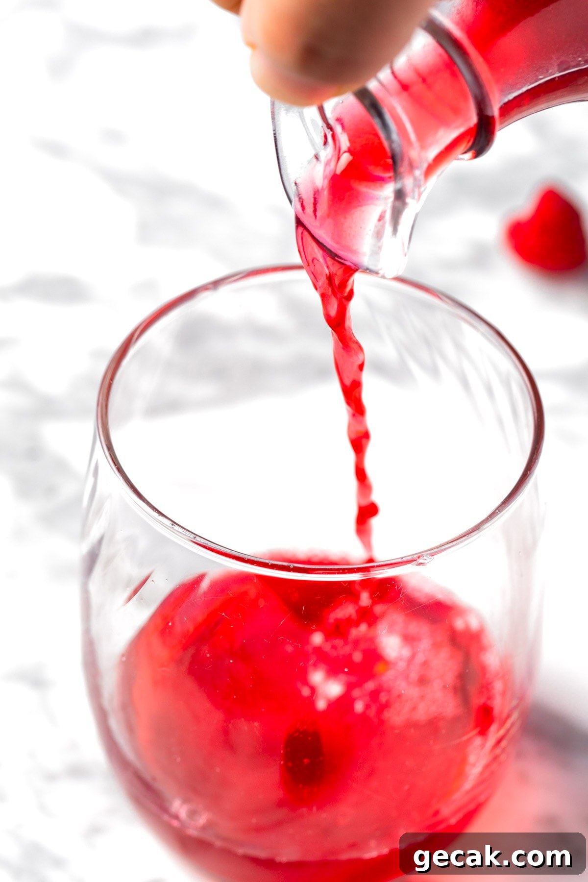 Homemade Raspberry Simple Syrup Recipe for Cocktails & Desserts 8 Raspberry syrup being poured into a glass, sitting on a white table.