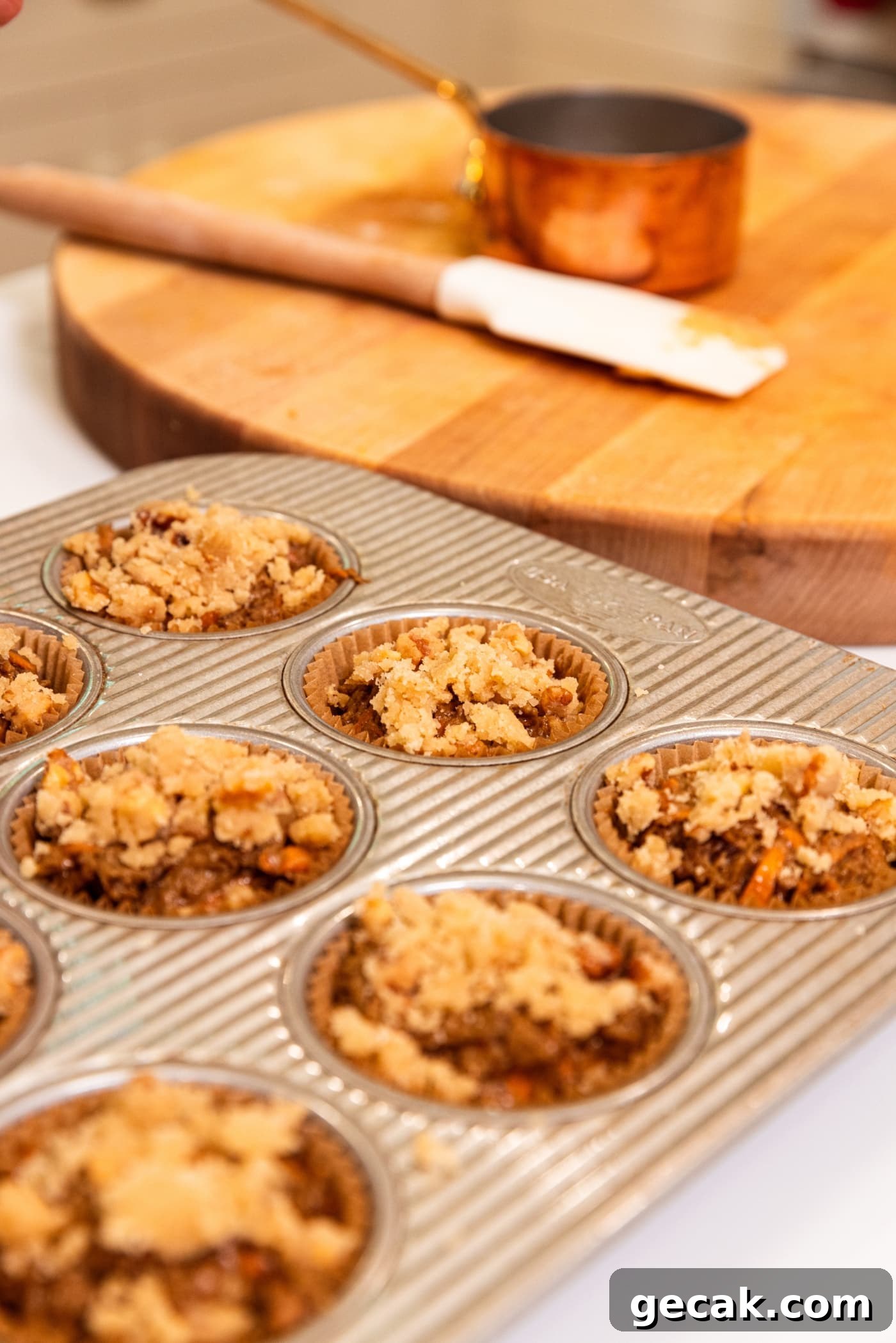 Streusel resting on top of unbaked muffins in muffin tin.