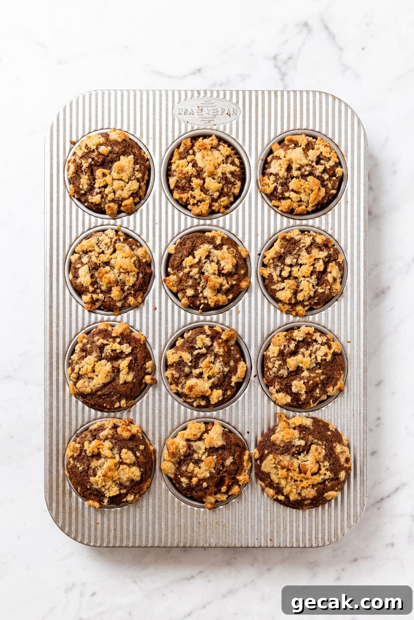 Metal muffin tin on white marble surface with baked spiced carrot muffins right after coming out of the oven.