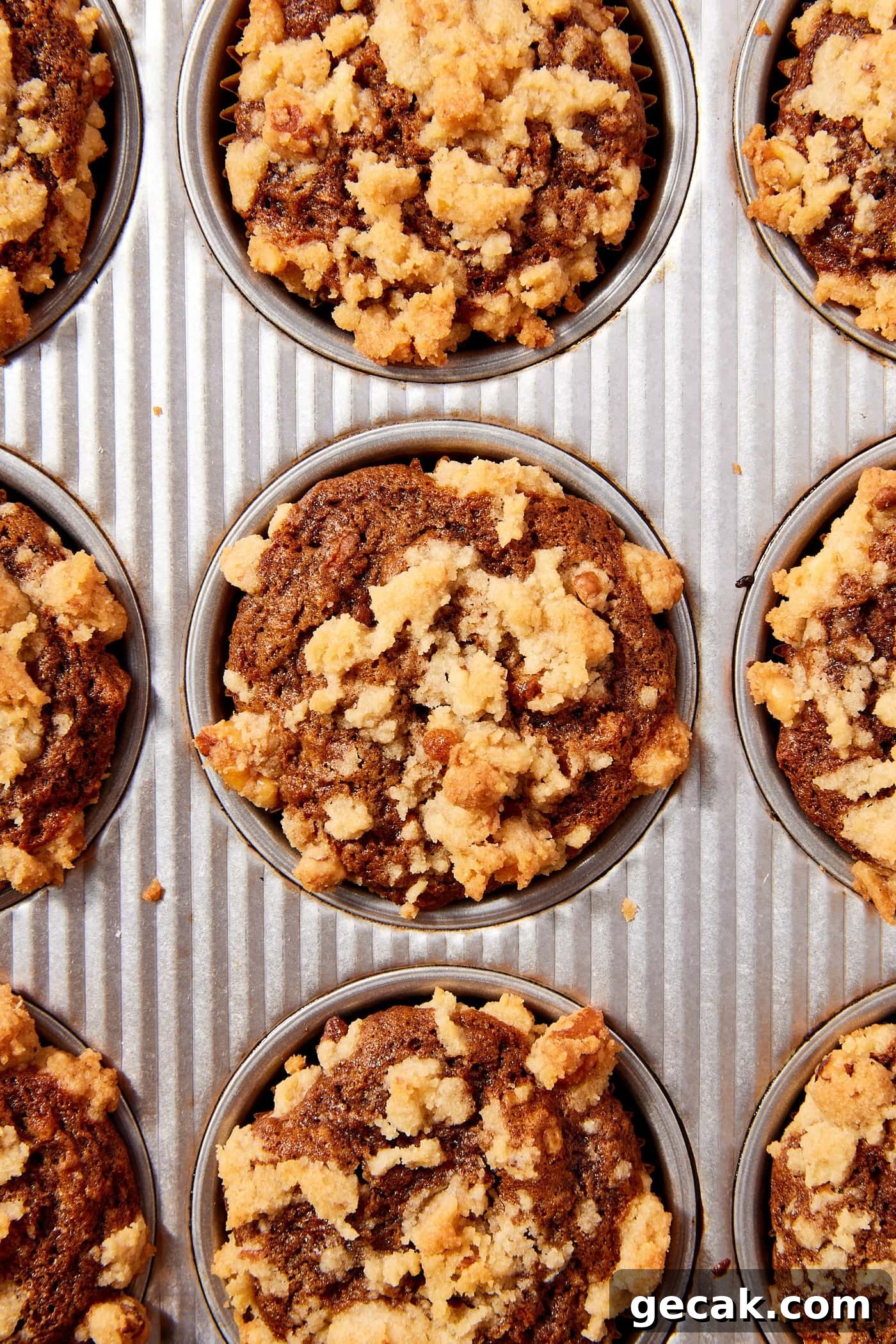 Metal baking pan filled with baked spiced carrot muffins with streusel topping all over.
