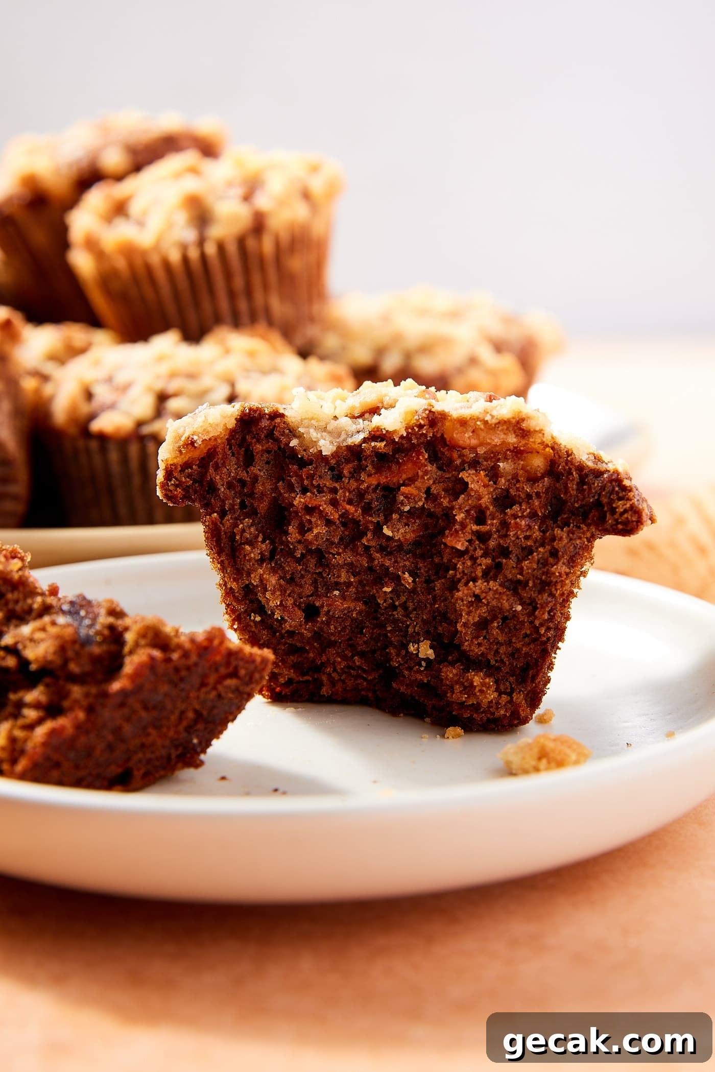 White plate with spiced carrot muffin sitting on it after being broken in half with dark interior texture and streusel topping.