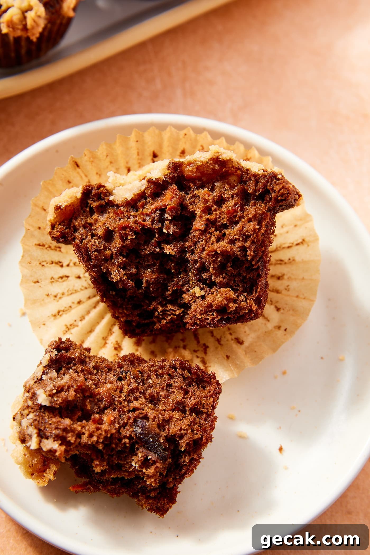 Dark colored spiced carrot muffin with streusel topping resting on plate after being torn in half to show interior.