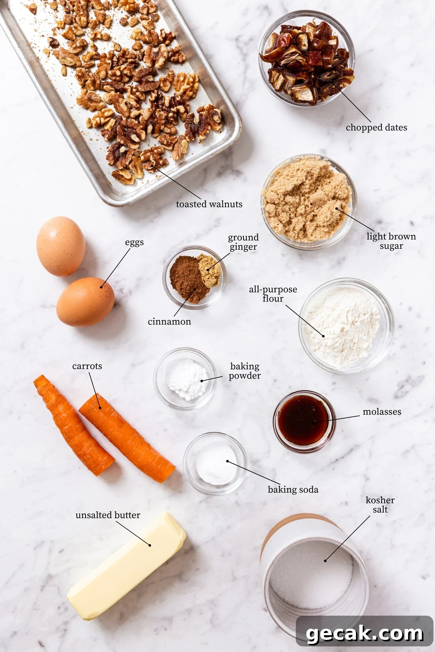 White marble surface filled with all ingredients needed to make spiced carrot muffins including raw carrot, walnuts, eggs, spices, and more.