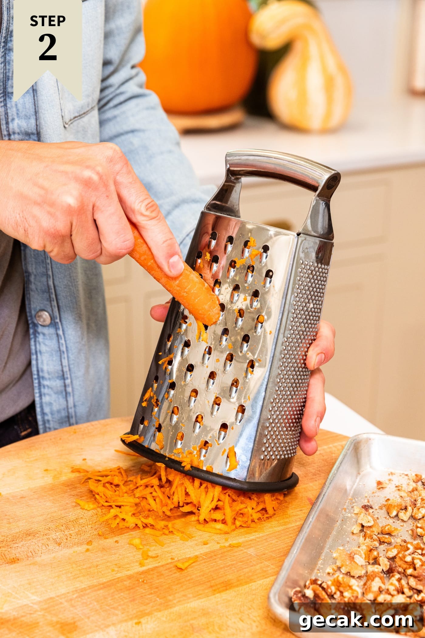 Hand grating carrot on grater onto wood cutting board with pieces of carrot underneath.