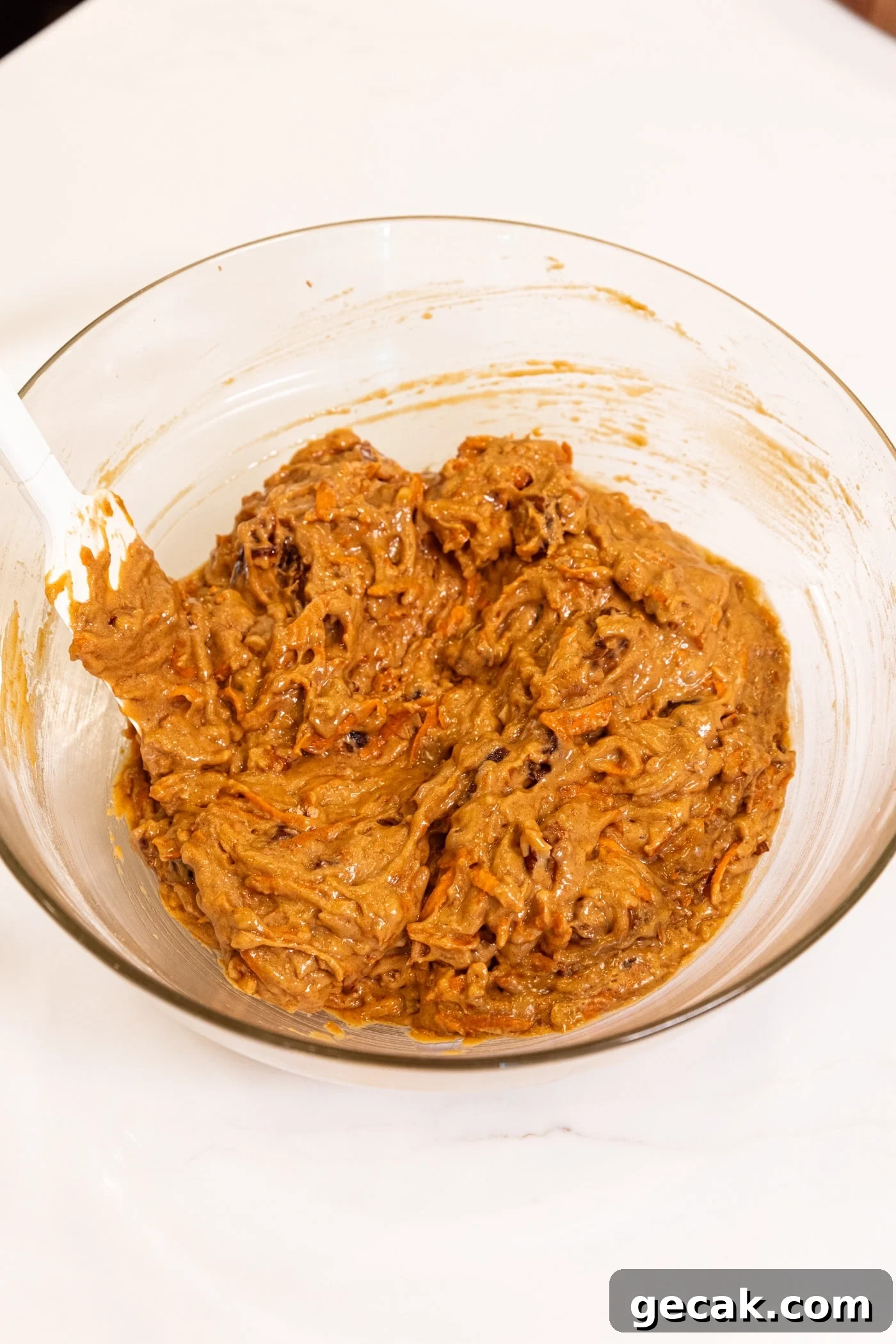 Plastic spatula resting in glass bowl with batter ready for spiced carrot muffins.
