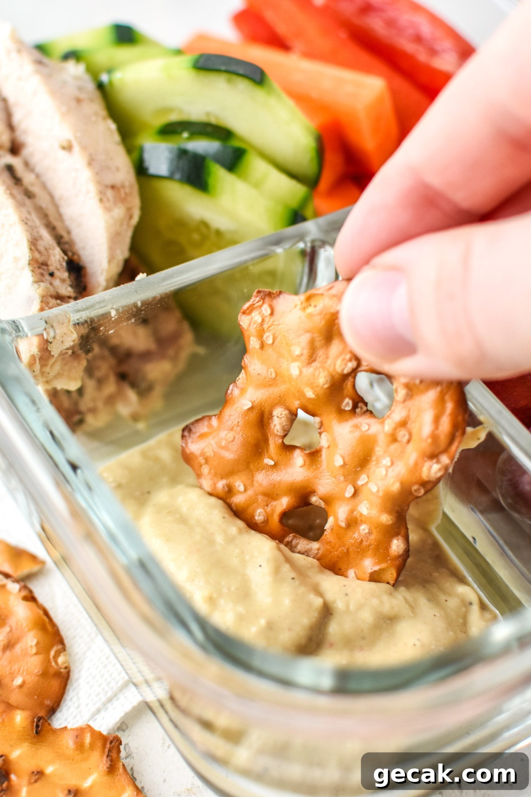 Dipping a pretzel into the hummus of the Chicken & Hummus Plate Lunch Meal Prep.