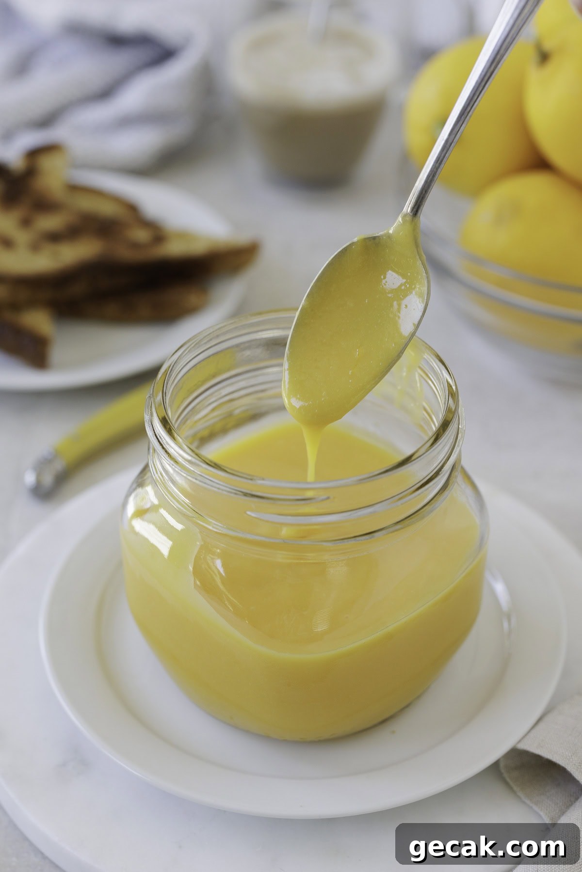 Creamy lemon curd dripping from a silver soon over a jar.