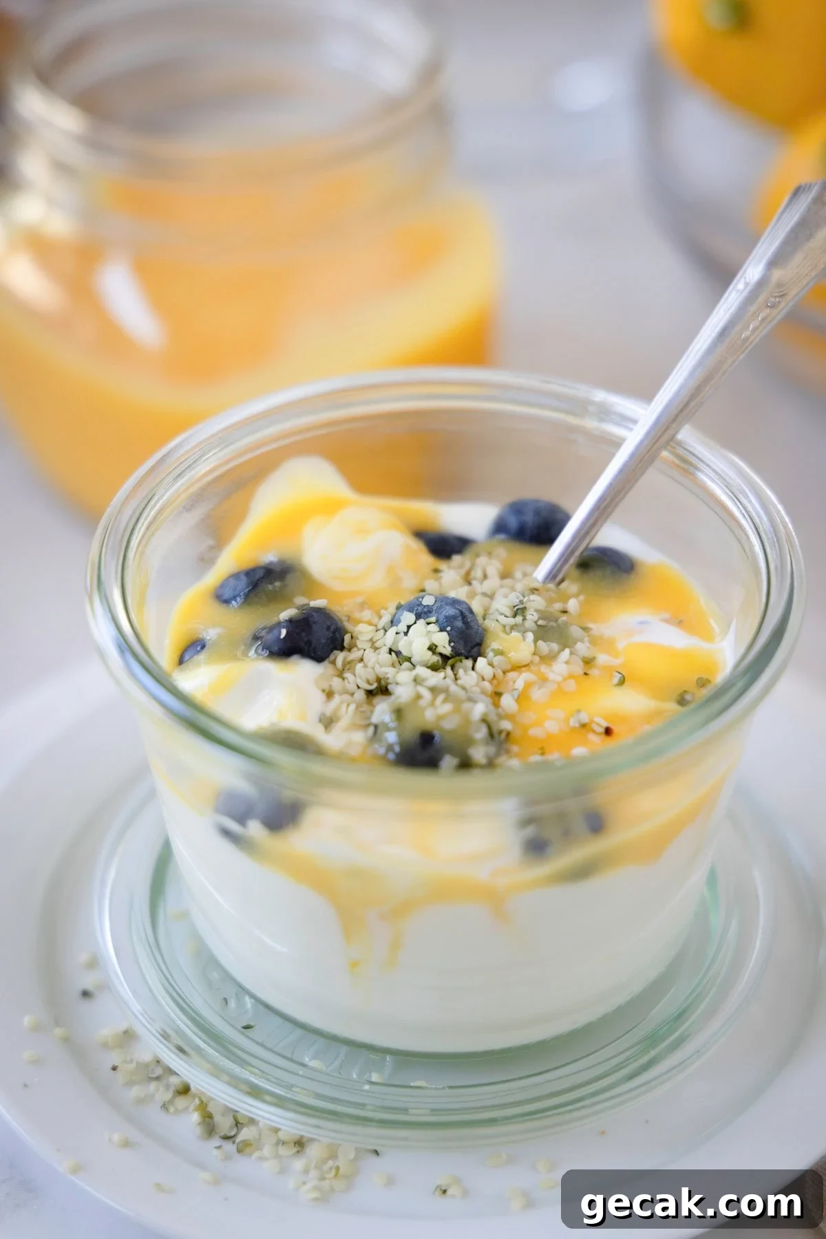 A jar of yogurt topped with lemon curd and fresh blueberries with a silver spoon.