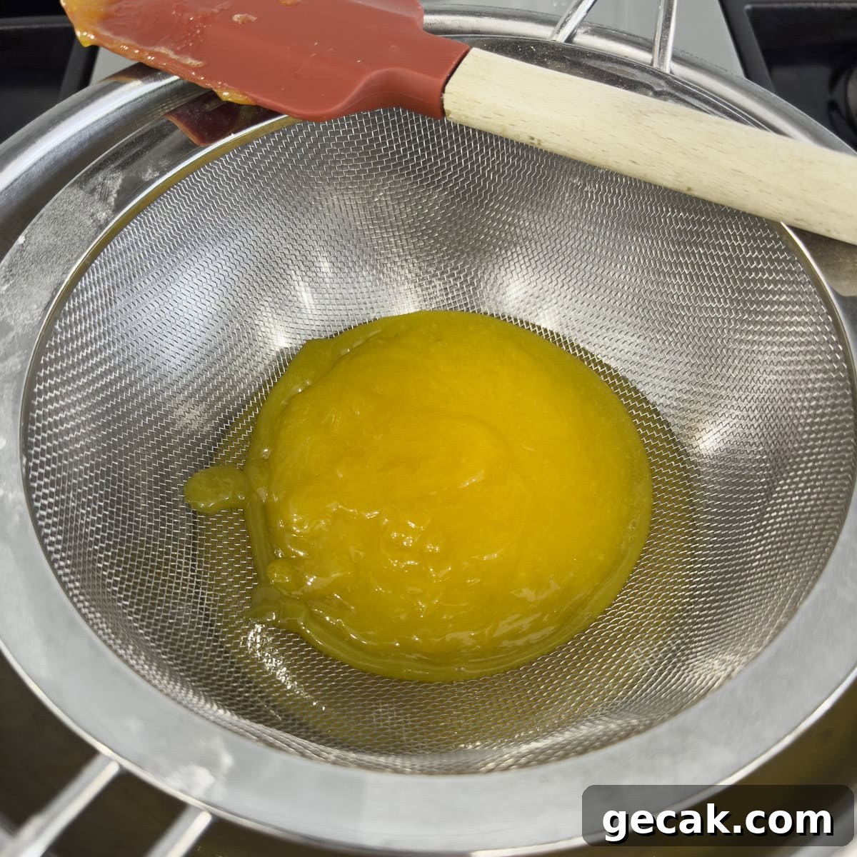 Straining cooked lemon curd through a sieve into a clean bowl.