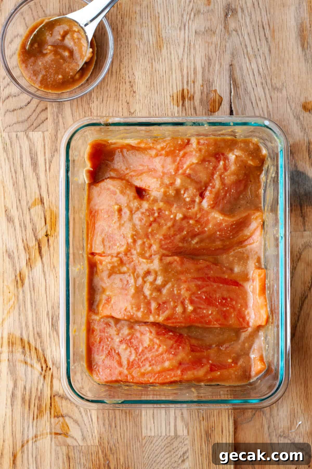 Four portions of salmon in a dish with miso marinade on a butcherblock countertop.