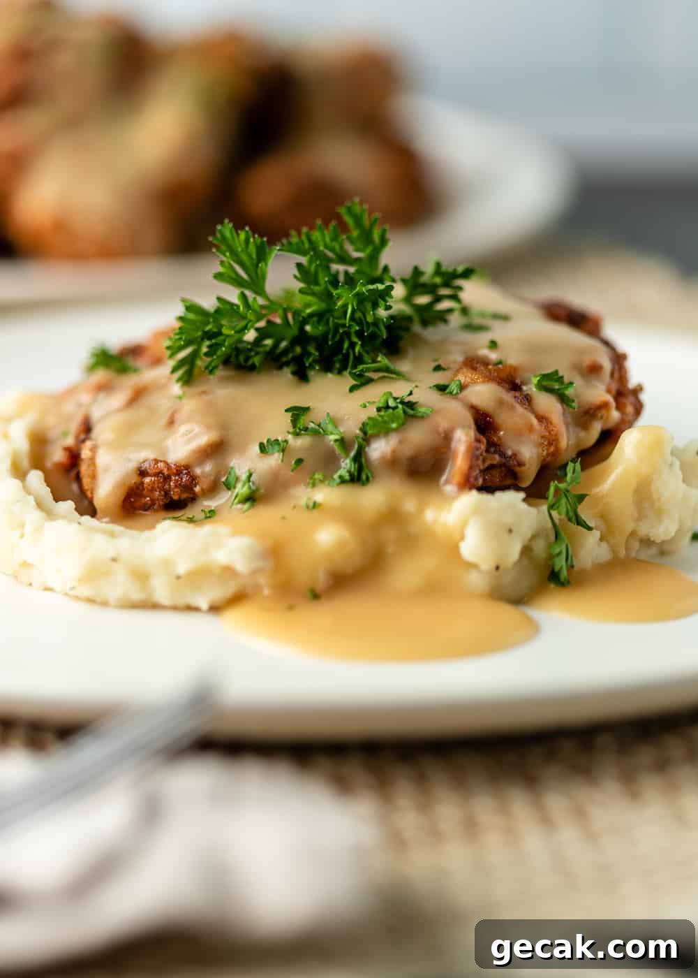 chicken fried steak with gravy on a plat ewith mashed potatoes and parsley sprig