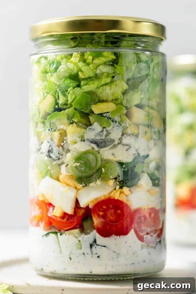 Dressing, tomatoes, hard-boiled eggs, cheese and lettuce layered in a jar.