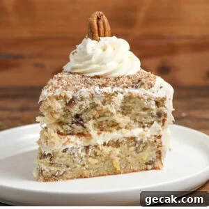 A slice of Italian cream cake with white frosting, topped with a swirl of frosting and a whole pecan, served on a white plate against a wooden background.
