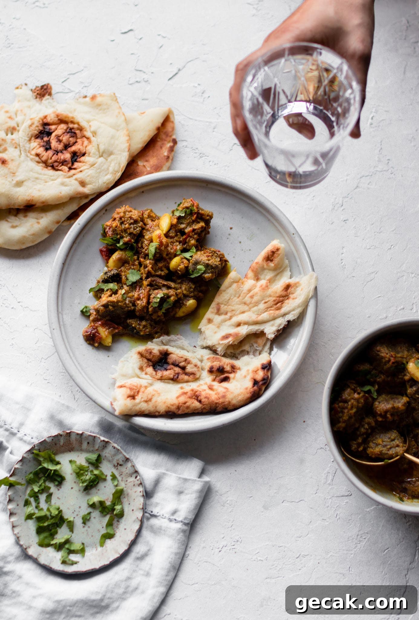 Picking up a glass of water above Pakistani-style Beef Curry (Stew) on a plate with naan