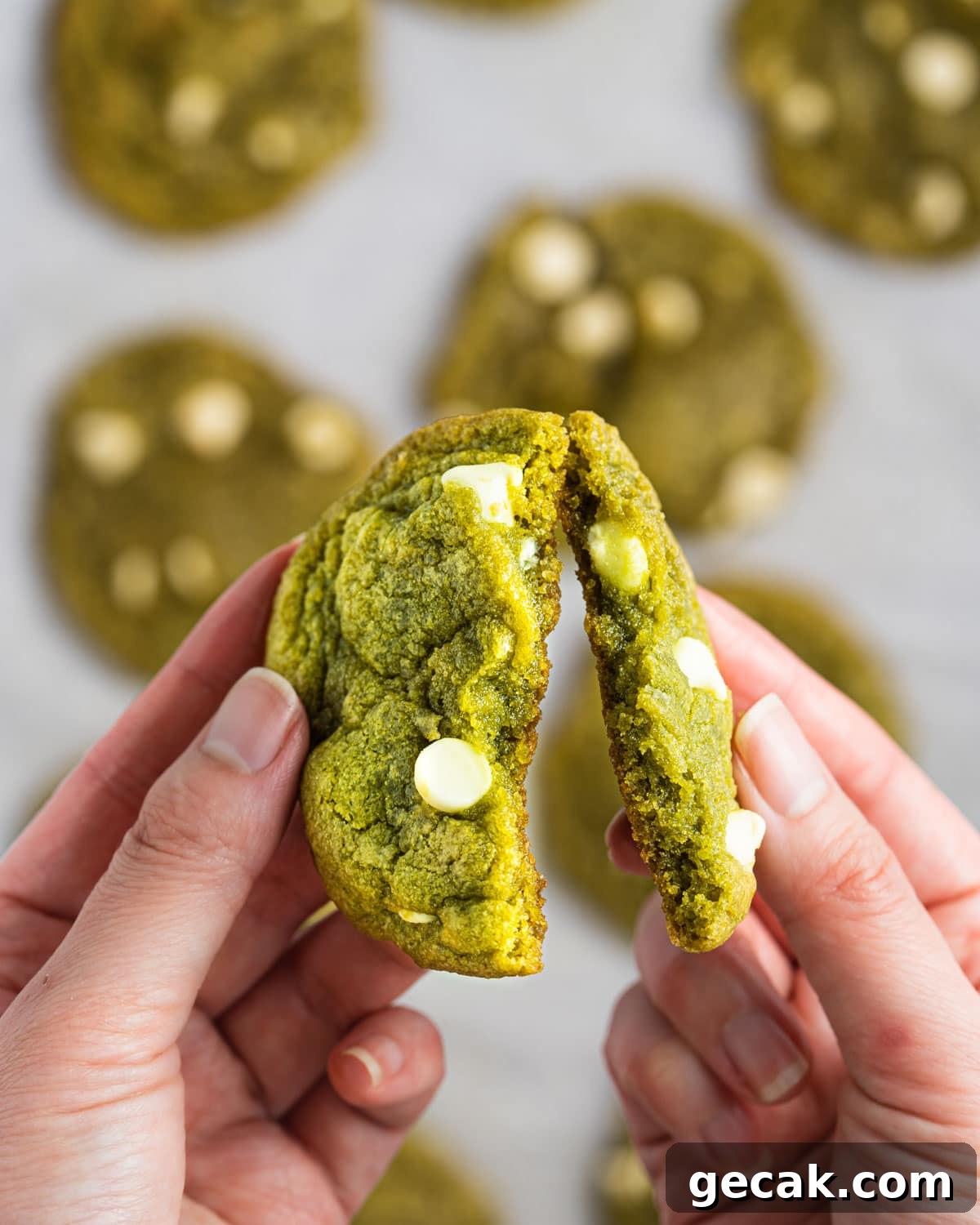 Hand breaking Matcha White Chocolate Chip Cookies apart.