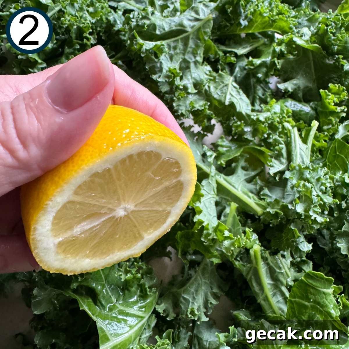 Hand holding half of a lemon over kale leaves.