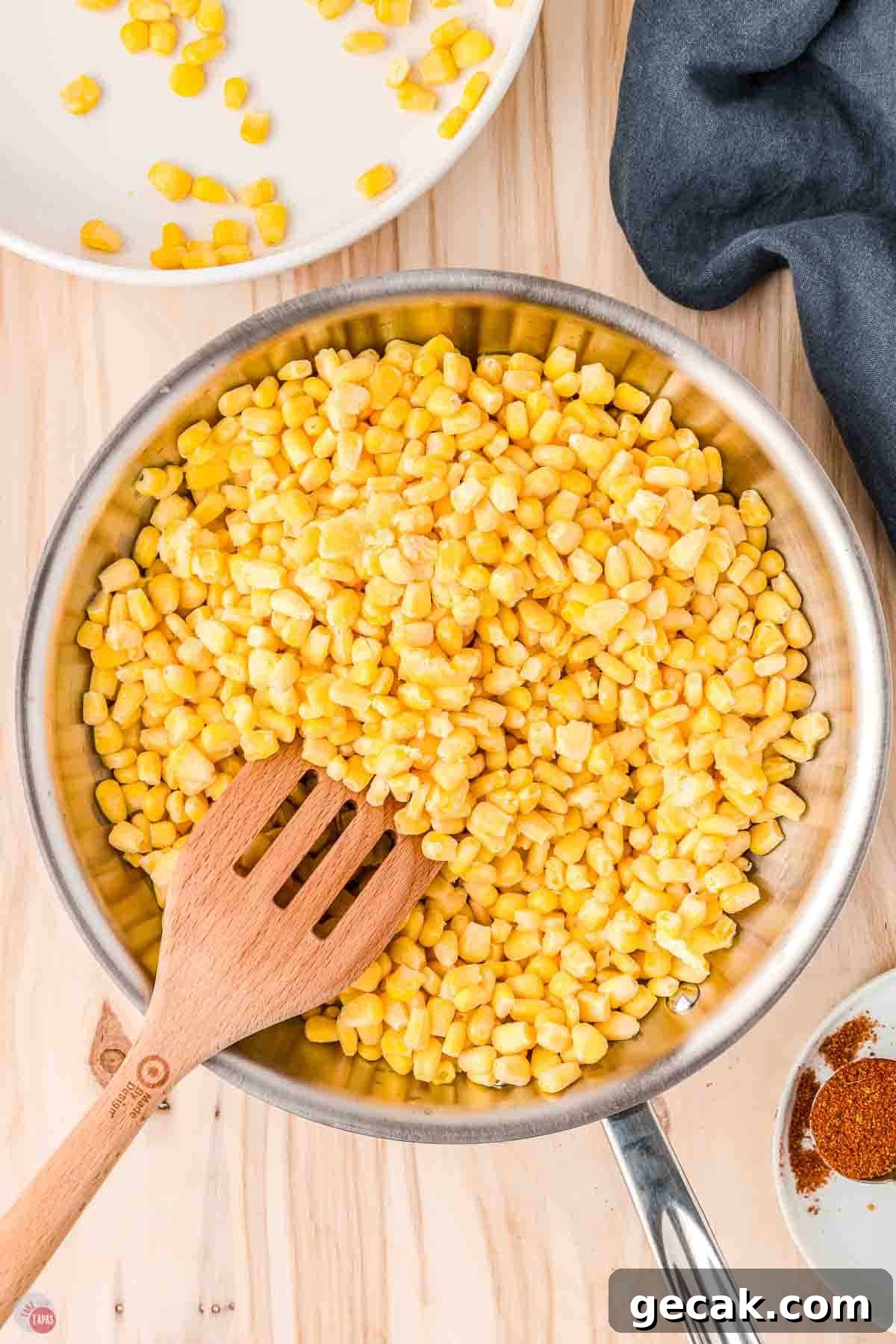 frozen corn kernels in a skillet with a slotted wood spatula