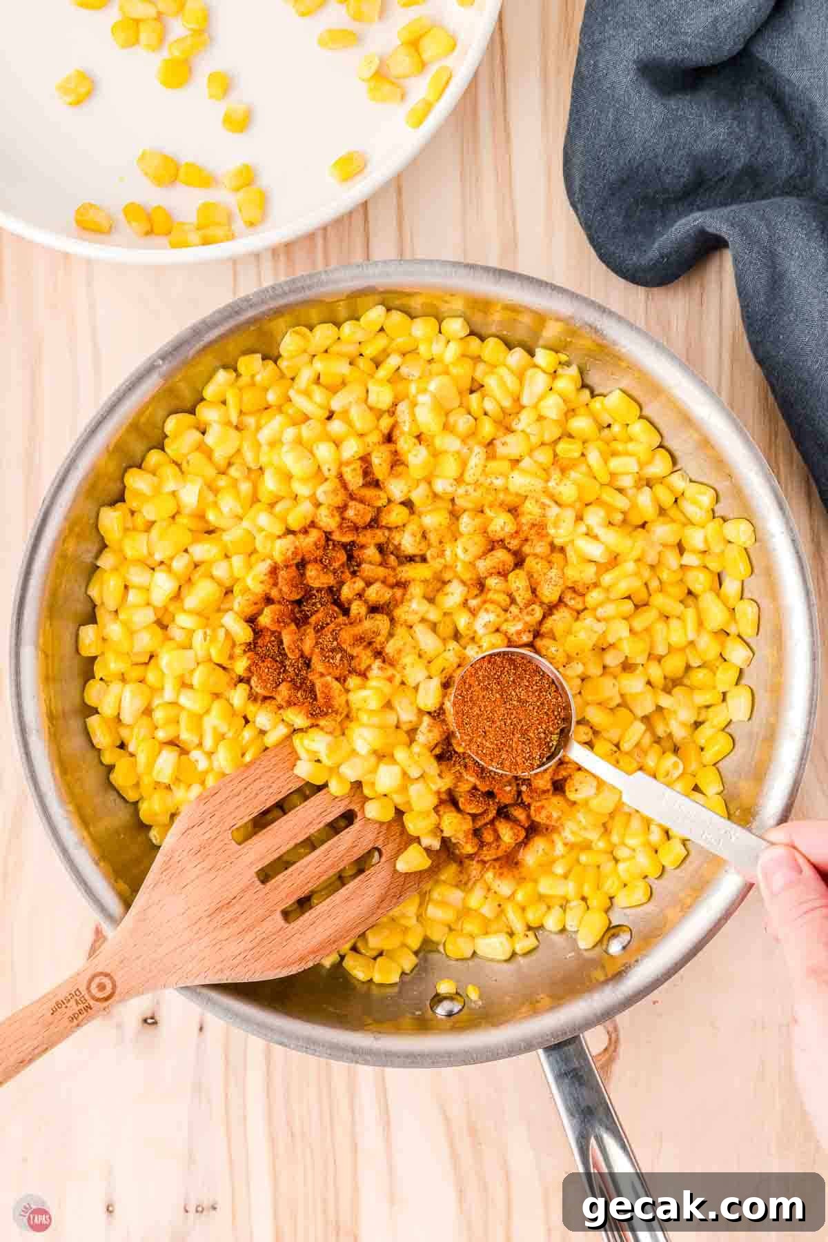 corn in a skillet with  a measuring spoon sprinkling seasoning on it