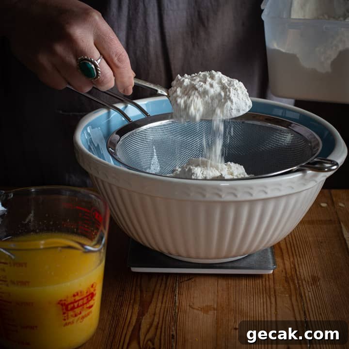 Chocolate Orange Muffins Recipe with Zesty Dark Chocolate Swirls 5 womans hand spooning flour into a blue and white mixing bowl on a wooden kitchen counter