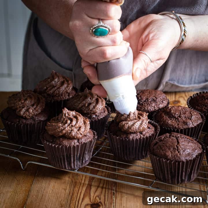 Chocolate Orange Muffins Recipe with Zesty Dark Chocolate Swirls 6 womans hand piping chocolate buttercream onto chocolate muffins