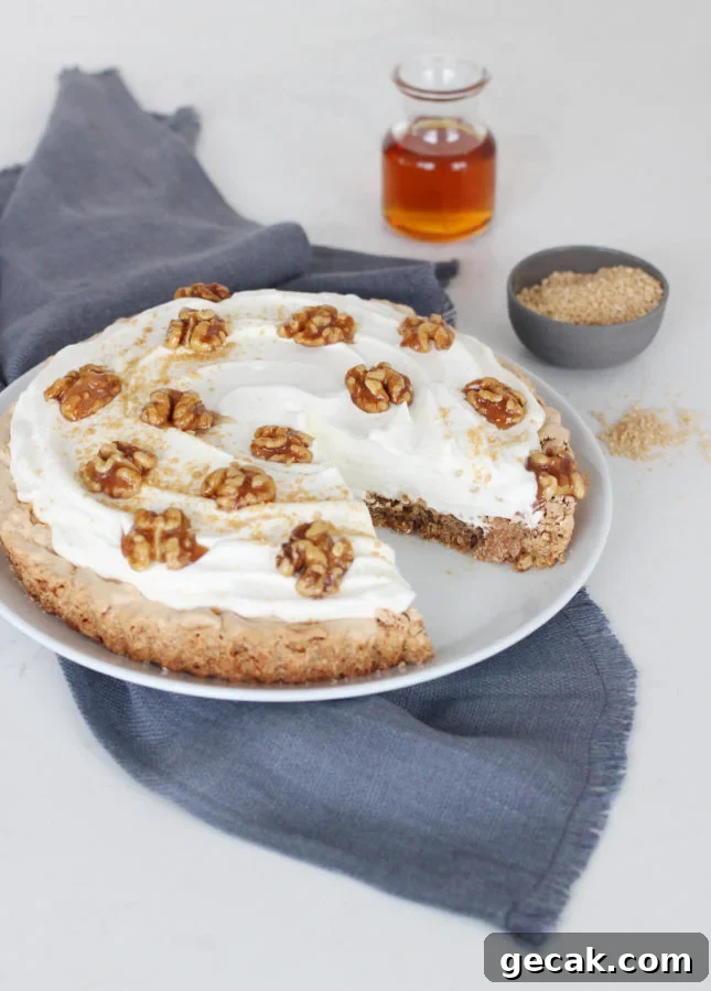 A maple cream tart topped with nuts and whipped cream sits on a white plate, with one slice missing.